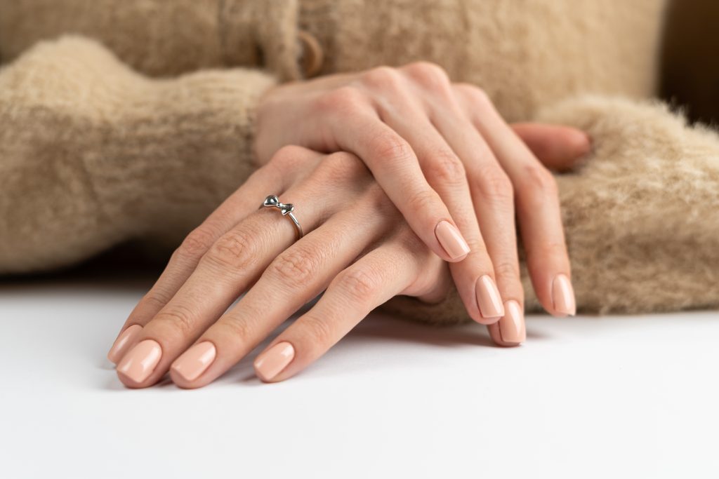 Doigts fins et gracieux d'une fille avec une manucure nude pastel très tendance, un pull doux et moelleux et un joli nœud de bague argenté.